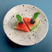 An Elite Global Solutions chocolate chip melamine plate with a watermelon slice and berries with mint leaves on a table.