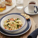 A Libbey Lunar Bright White porcelain saucer with a steel blue band on a table with a bowl of pasta.