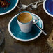 A Villeroy & Boch Pacific Green porcelain cup of coffee on a saucer with a spoon.