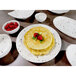 A white melamine bowl with brown specks filled with a stack of pancakes and raspberries.