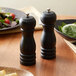 Two Acopa matte black wooden salt and pepper mills on a table with food.