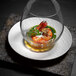 A glass bowl with food on a white Villeroy & Boch porcelain plate with a shrimp on top.