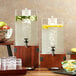 A walnut square riser holding an acrylic beverage dispenser filled with water and lemon slices.