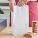 A hand holding a Choice white waxed paper bag filled with food.