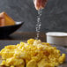 A hand sprinkling Regal Fine Sea Salt on a plate of scrambled eggs.