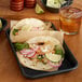 A Baker's Mark black wire rim aluminum sheet tray holding two tacos with chicken, lettuce, and salsa.