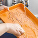 A person washing a Baker's Mark orange wire-in-rim aluminum sheet tray on a counter.