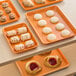 A Baker's Mark orange wire in rim aluminum tray holding a variety of pastries on a table.