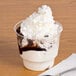 A Solo clear sundae cup filled with ice cream, whipped cream, and chocolate sauce with a spoon.