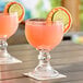 Two Acopa schooner glasses filled with pink drinks and lime slices on top.