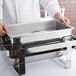 A chef holding a Vollrath stainless steel water pan over a counter.