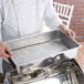 A person holding a Vollrath stainless steel water pan lid.