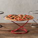 An American Metalcraft red wrought iron swirl display stand with a pizza on it.