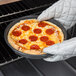 A person in gloves holding a Chicago Metallic deep dish pizza in an oven.