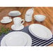 A table set with a stack of white Elite Global Solutions melamine bowls, plates, and cups.