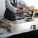 A man using a Carnival King Deluxe Butane Made-To-Order Crepe Station to cook food on a table in a hotel buffet.