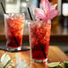 Two glasses of Monin hibiscus flavored red liquid with flowers on top.