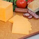 A cutting board with Yellow Mild Cheddar Cheese, tomatoes, and bread.