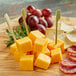 Cubed Yellow Cheddar cheese with grapes on a wooden board.