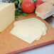 A cutting board with Pearl Valley Lacey Swiss Cheese, tomatoes, and bread. 