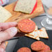 A hand holding a cracker with a slice of Hormel pepperoni on top.