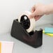 A hand using a Shurtape 3" masking tape dispenser to tape paper.
