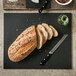 A loaf of bread with seeds being sliced on an Epicurean Richlite wood fiber cutting board.