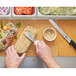 A person's hands using a knife to cut a sandwich on a Epicurean PuzzleBoard.