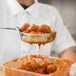 A person using a Vollrath Orange Perforated Spoodle to serve meatballs.