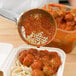 A Vollrath orange perforated round Spoodle pouring sauce over a bowl of spaghetti with meatballs.