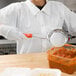 A person using a Vollrath Orange Perforated Spoodle to serve sauce.