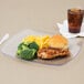 A Fineline clear plastic plate with a sandwich and broccoli on it next to a glass of brown liquid with ice.