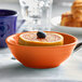 An orange bowl with a Tuxton Concentrix Papaya Nappie Bowl filled with orange slices and a blueberry.
