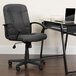 A Flash Furniture gray office chair with nylon arms next to a glass desk with a laptop on it.
