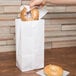 A hand holding a bagel in a Duro white paper bag.