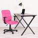 A Flash Furniture pink mid-back office chair with armrests next to a black desk with a laptop on it.