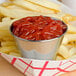 A stainless steel round sauce cup filled with ketchup next to french fries.