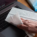 A hand using a Windex electronics cleaner wipe to clean a laptop keyboard.