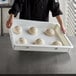 A person holding a Baker's Mark white heavy-duty polypropylene dough proofing tray with dough balls.