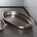 An American Metalcraft stainless steel oval serving pan on a metal surface with a spoon.