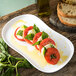 A Carlisle white melamine platter with tomatoes, basil, and bread on it.