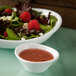 A bowl of salad with raspberries and a Carlisle white melamine sauce cup filled with red sauce.