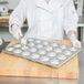 A person in a white coat pouring liquid into a Chicago Metallic muffin tin.
