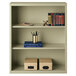 A Hirsh putty steel bookcase with shelves of books and pens.