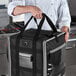 A chef holding a black and grey Vollrath delivery backpack bag.