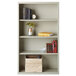 A light gray Hirsh welded steel bookcase with books and a vase of flowers on top.