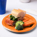 A sandwich with lettuce, cheese, carrots, and broccoli on a Sunkissed orange plastic plate.