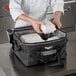 A chef holding a white Vollrath insulated food pan carrier with food in it.