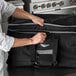 A person opening a black Vollrath 3-Series large insulated food pan carrier bag.