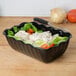 A black Cambro deli crock filled with lettuce, tomatoes, and tuna salad on a salad bar counter.